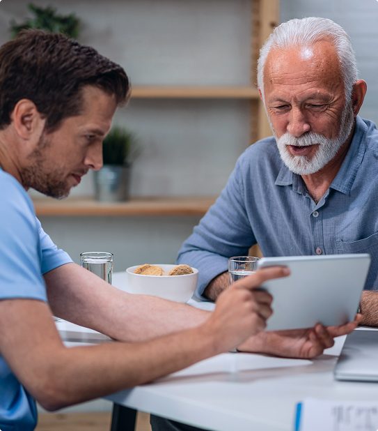 Caregiver reviewing information on a tablet with an elderly man at home